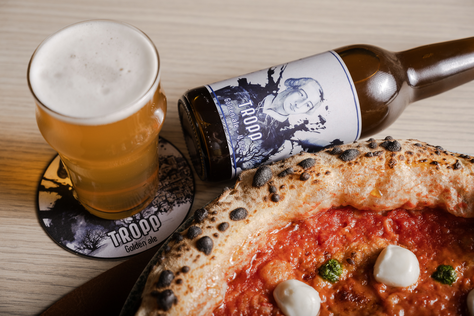 Pizza di Tropp con pomodoro e mozzarella accanto a un bicchiere e una bottiglia di birra Tropp